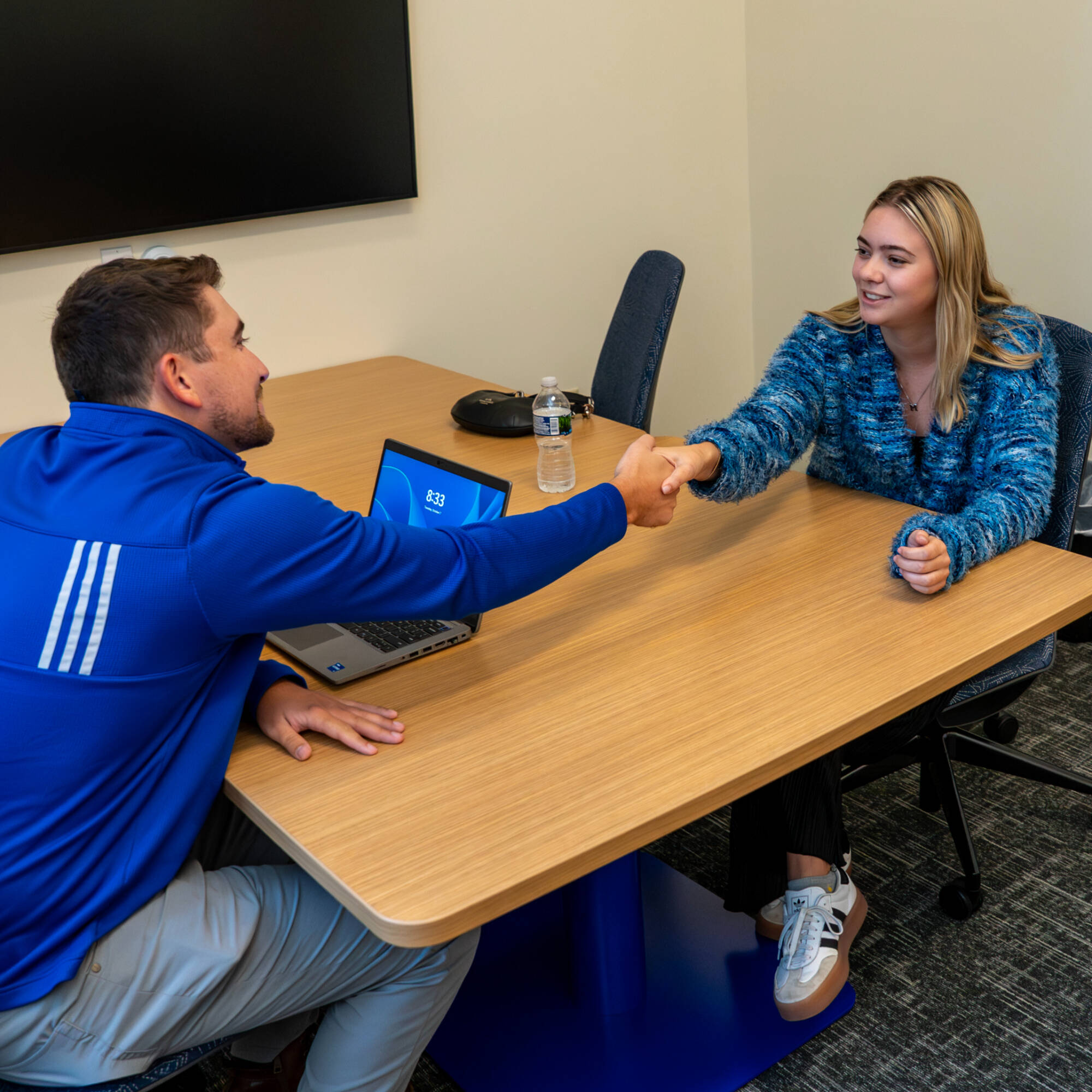 Two students shaking hands in one of the breakout rooms in the sales lab